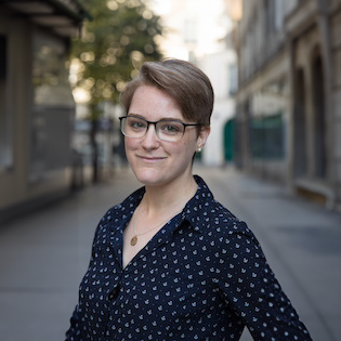 Professional headshot of Magali Ferare, she's standing in a parisian street, smiling and looks energetic